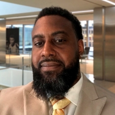 Max Bazile portrait of a man wtih dark hair and beard, wearing a white shirt, beige suit, and pale yellow tie
