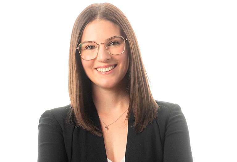 Adriane MacDonald. | Photo : David Ward Jeune femme souriante avec des lunettes, des cheveux longs, noirs et raides, et portant un blazer sombre.